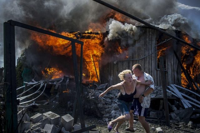 Mense vlug uit 'n huis wat aan die brand geslaan het na 'n lugaanval deur terroriste in die Luhanskaya-dorpie (Foto: Valery Melnikov/Rossia Segodnya)